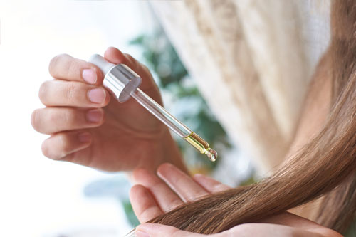 woman-putting-essential-oils-on-her-hair-with-dropper